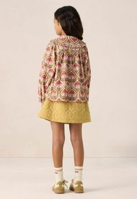 Floral-patterned, pink blouse with ruffled collar, paired with a quilted yellow skirt. Tan shoes with accents and heart-patterned socks visible.