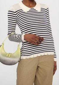 Námořnický a bílý pruhovaný svetr s dlouhým rukávem a vlnitým límcem, doplněný kabelkou ve žluto-šedém gradientu a béžovými kalhotami.