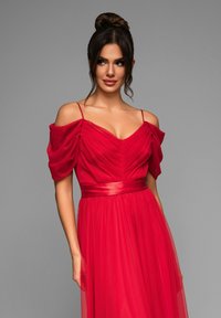 Robe de soir�ée rouge avec des manches dénudées, un corsage plissé et une ceinture en satin. Fabriquée en tissu fluide avec une jupe superposée et légère.