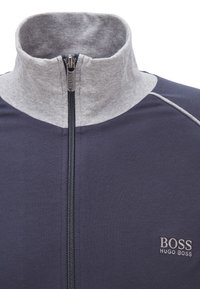 Navy blue jacket with light grey high collar, full front zipper, and "BOSS HUGO BOSS" logo embroidered on chest.