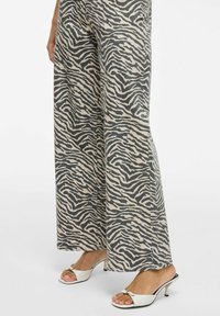 Kankurihousut vaaleassa kankaassa, jossa on musta seepraraidallinen kuvio. Yhdistetty valkoisiin avonaisiin korkokenkiin, joissa on metallinen yksityiskohta.