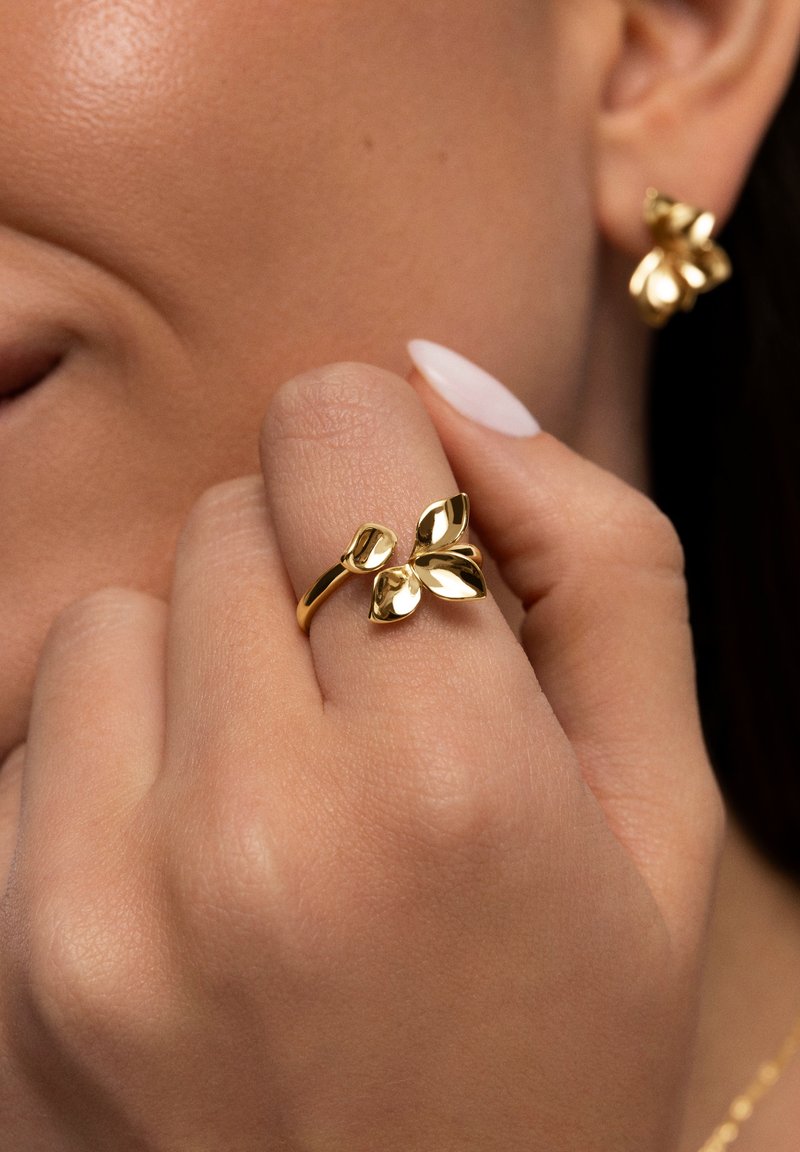 Goldring mit floralen Motiven und drei blütenblattähnlichen Akzenten, präsentiert vor einer Hand mit natürlicher Hautstruktur und einem hellen Nagellack.