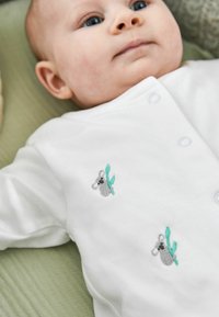 Weißer Baby-Body mit grauem Koala und grüner Blattstickerei. Weicher Stoff, mit Druckknöpfen an der Seite für einfaches Ankleiden.