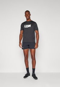 Fekete sportpóló "LDN" felirattal, fekete rövidnadrággal párosítva. Simább textúrával, laza fazonnal rendelkezik, és fekete sportcipővel viselik.