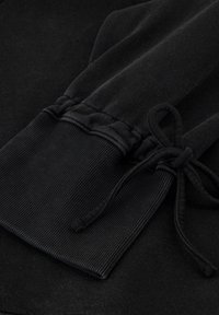 Zwarte sweatshirtstof met ribbelmanchetten, voorzien van een trekkoordsluiting. Soepele textuur met een geraffineerde afwerking bij de pols.