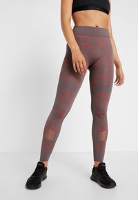 Leggings made of stretchy gray fabric with red camouflage pattern, featuring mesh accents on the lower legs and a high waistband.
