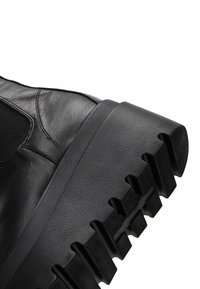 Black leather boot featuring a high ankle design, textured upper, and sturdy rubber sole with pronounced ridges for traction.