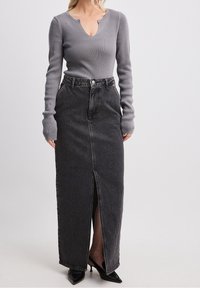 Harmaa ribbineulottu pitkähihaisen paita V-aukkolla, yhdistettynä mustaan farkkumaxihameeseen, jossa on etuslitsi ja taskudetaljit. Mustat kärjestä terävät korkokengät.