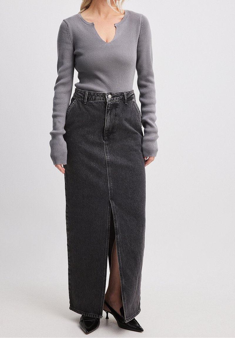 Harmaa ribbineulottu pitkähihaisen paita V-aukkolla, yhdistettynä mustaan farkkumaxihameeseen, jossa on etuslitsi ja taskudetaljit. Mustat kärjestä terävät korkokengät.