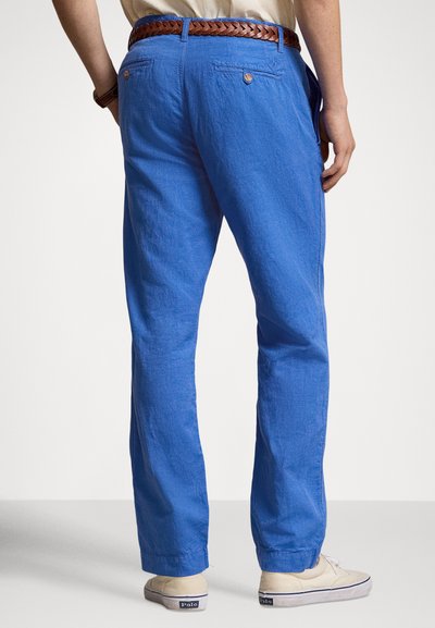 Μπλε παντελόνι από λινό με άνετη εφαρμογή, διαθέτει δύο πίσω τσέπες και πλεκτή καφέ δερμάτινη ζώνη. Το σύνολο ολοκληρώνουν ανοιχτόχρωμα casual παπούτσια.