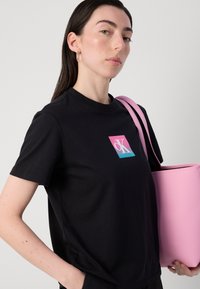 Black cotton t-shirt with short sleeves and a colored square logo. Features a pink tote bag with a smooth texture and round shape.