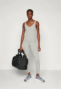 Grå trenings tank top og tights, parret med grå joggesko. Svart duffel bag med dobbelthåndtak. Glatt tekstur, tettsittende design.