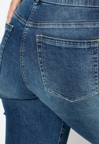 Niebieskie dżinsy o dopasowanym kroju, z kontrastowym przeszyciem, tylnymi kieszeniami i średnio wypranym teksture.