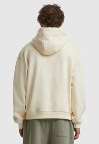 Cremefarbener Hoodie mit Kapuze und Kordelzug, überschnittenen Schultern und gerippten Bündchen. Weicher Stoff mit glatter Textur.