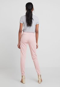 Lichtroze joggers met een trekkoord in de taille, zachte textuur en achterzakken, gecombineerd met een grijs T-shirt met korte mouwen. Hakken.