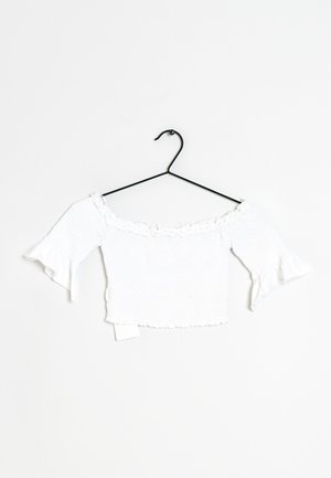 Top corto blanco, sin mangas, con textura fruncida, cuello con volantitos y mangas acampanadas, exhibido en un perchero negro.