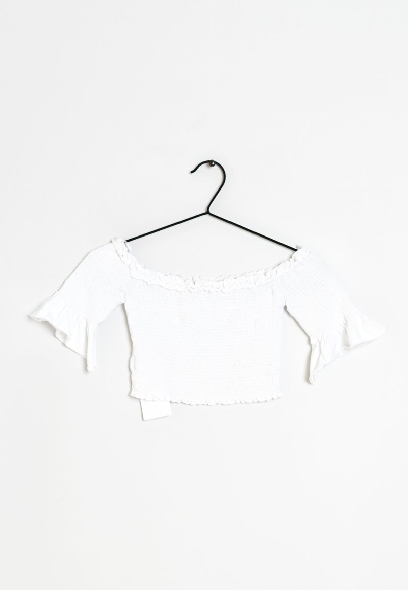 Weißes, schulterfreies Crop-Top mit geraffter Textur, Rüschensaum und ausladenden Ärmeln, auf einem schwarzen Kleiderbügel präsentiert.