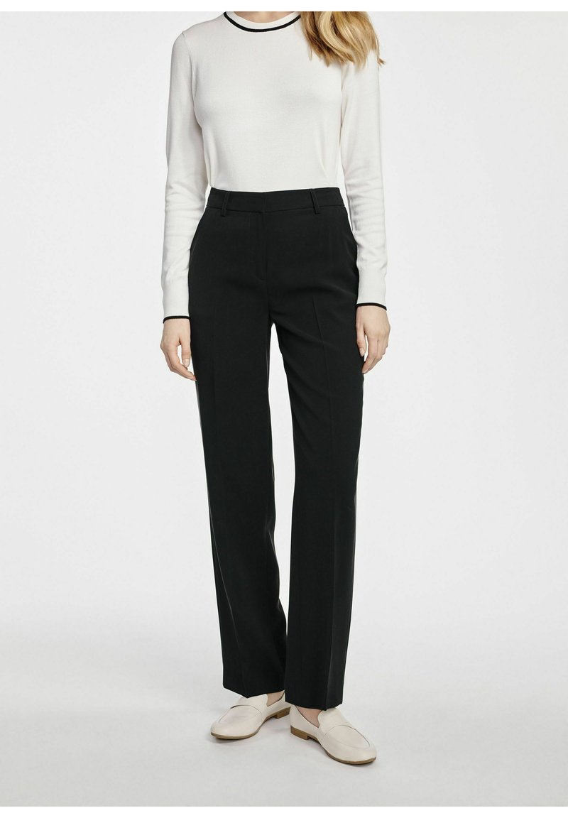 Czarne klasyczne spodnie z przednimi szwami, zestawione z białą bluzką z długim rękawem z czarnym dekoltem oraz jasnymi butami wsuwanymi.