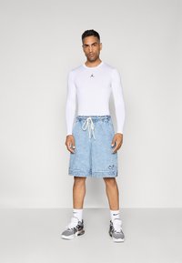 Hvid langærmet top med sort logo, lyseblå denim shorts med snoretræk og sorte sneakers med hvide detaljer.