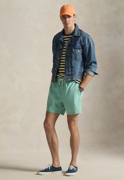 Τζιν μπουφάν, ριγέ μπλουζάκι, σορτς σε μέντα πράσινο και μπλε αθλητικά παπούτσια· πορτοκαλί καπέλο με λογότυπο· καθημερινό σύνολο με αντιθετικά χρώματα.