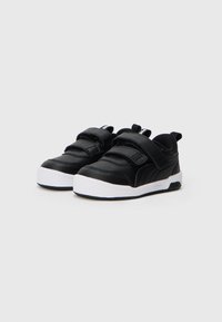 Baskets noires pour enfants avec semelles blanches et deux sangles velcro sur un fond clair uni, vue en angle.