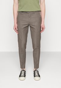 Pantalon marron sur mesure avec un motif à rayures subtiles, coupe slim, et poches avant classiques, accompagné de baskets noires avec des lacets blancs.