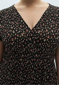 Schwarzes Kleid mit kleinem roten und grünen Blumenmuster, mit V-Ausschnitt und plissierter Textur, das einen fließenden und leichten Stoff betont.