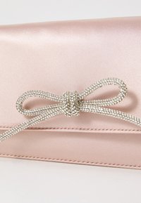 Pochette en satin rose avec un détail de nœud en strass argenté à l'avant. Le sac présente des lignes épurées et une couture minimaliste.