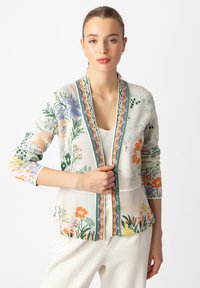 Cardigan floreale realizzato in un tessuto beige chiaro, con intricati motivi verdi, arancioni e viola, e un bordo multicolore lungo i contorni.