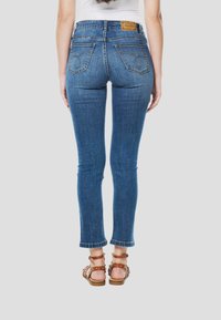 Skinny jeans in mediumblauwe denim met een hoge taille, achterzakken met stikseldetails en een rafelige zoom. Bruine sandalen met bandjes.