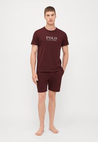 Bordo majica s kratkim rukavima i odgovarajuće šortse, napravljeni od mekog materijala, s bijelim logom "POLO RALPH LAUREN" na prednjoj strani.