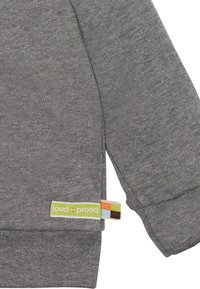 Grauer Sweatshirt aus strukturiertem Stoff mit einem Etikett, auf dem "loud + proud" in Grün steht, akzentuiert mit orangen, blauen und braunen Quadraten.