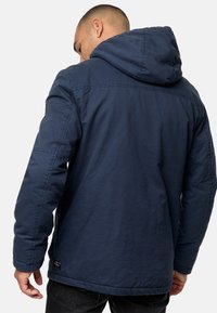 Marineblauwe hoodie met een gestructureerde stof, zichtbare stiksels en een logo-opnaad op de schouder. Eenvoudige achterkant met een relaxte pasvorm.