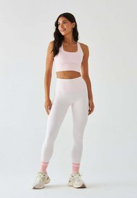Jasnoróżowy sportowy biustonosz i legginsy z wysokim stanem wykonane z elastycznej tkaniny, charakteryzujące się gładką fakturą i krojem o długości do talii.