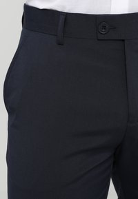 Marineblaue Hose aus glattem Stoff, ausgestattet mit einem Knopfverschluss und Gürtelschlaufen, mit seitlichen Taschen und maßgeschneiderter Passform.