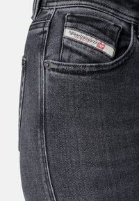 Jeans de mezclilla negros con una textura sutil, que cuentan con una etiqueta de bolsillo de Diesel y costuras en contraste. Incluyen un detalle de botón metálico.
