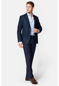 Granatowa marynarka z brązowymi guzikami, w połączeniu z niebieską i białą koszulą w paski oraz ciemnymi spodniami. Noszone są brązowe skórzane buty.