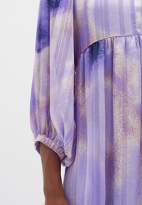 Purple patterned dress with sheer fabric, featuring billowy long sleeves and gathered waist, showcasing a mix of light and dark tones.