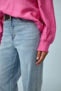 Rosa Langarmshirt mit gerafften Bündchen, kombiniert mit hellblauen hoch taillierten Jeans, die eine lockere Passform und Denim-Textur zeigen.