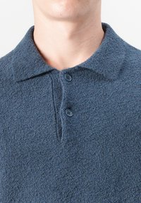 Camisa polo azul marino hecha de tejido texturizado, con un cierre de botones y un diseño de cuello clásico. Superficie suave y ajuste casual.