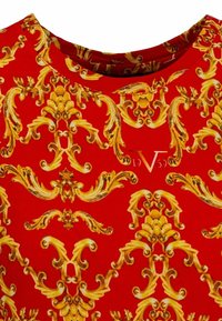 Rode top met een ingewikkeld gouden barokpatroon. Zachte stof met een ronde hals. Een klein logo is zichtbaar nabij de halslijn.