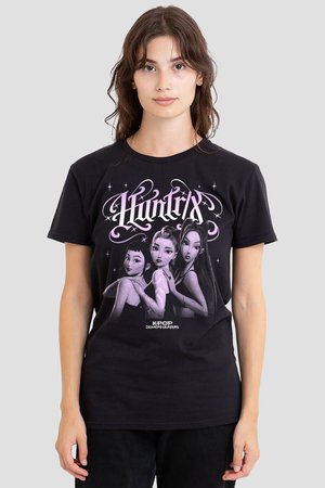 Junge Frau trägt ein schwarzes T-Shirt mit drei animierten weiblichen Charakteren und den Worten "HUNTRIX" und "KPOP DEMON HUNTERS".