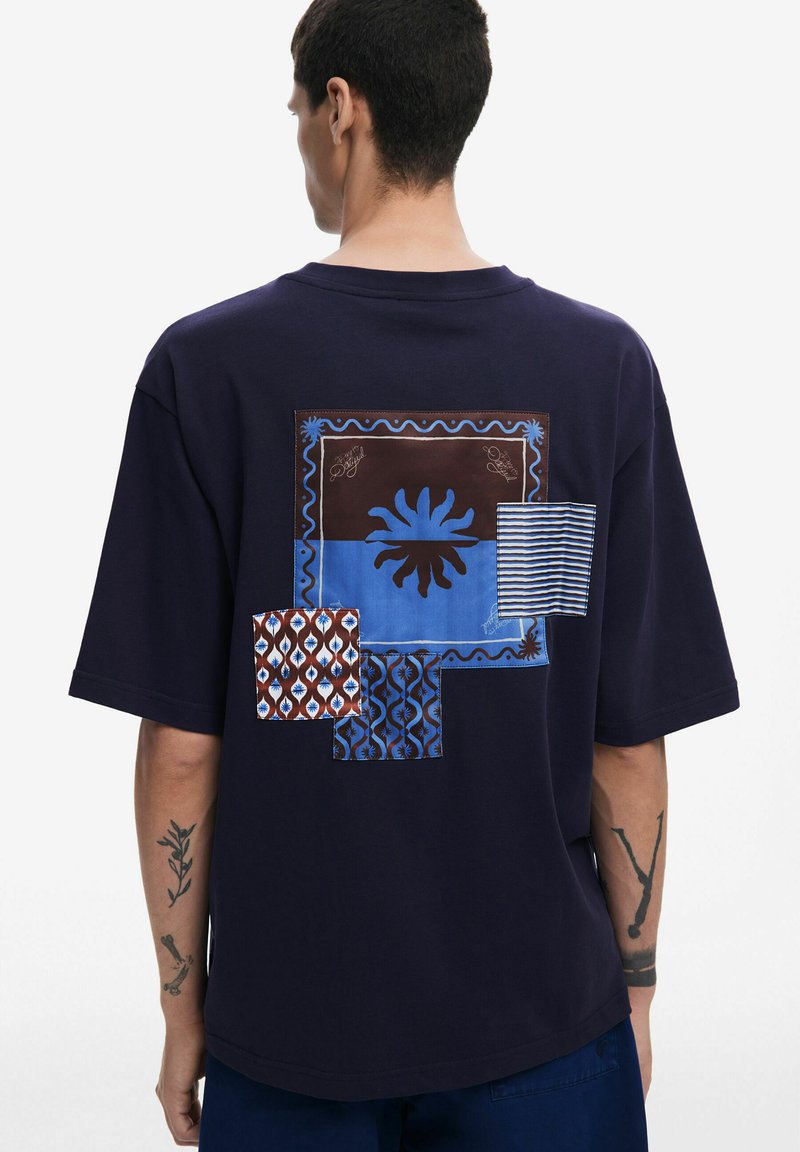 Camiseta de manga corta en color navy con un gráfico de múltiples patrones en la parte trasera que incluye acentos en azul y marrón, con diseños geométricos y rayas.