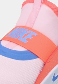 Scarpa slip-on Nike con tomaia in maglia rosa, cinturino arancione con marchio blu e tallone blu a contrasto. Texture liscia e forma arrotondata.