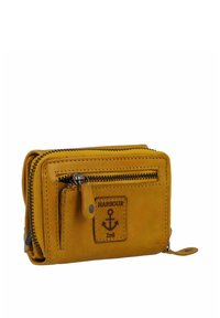 Cartera de piel amarilla con cierre de cremallera, que presenta un diseño de ancla y una etiqueta de marca, múltiples compartimentos y una textura suave.