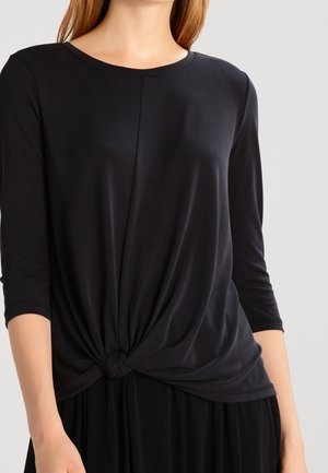 Maglia nera a maniche lunghe realizzata in tessuto morbido e elastico; presenta un dettaglio annodato in vita e un collo rotondo.
