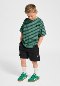 Grön randig t-shirt med rund hals, svart logotyp, svarta shorts och gröna sneakers med vita detaljer och kardborreband.