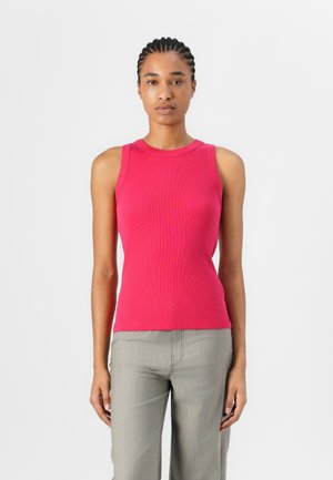 Fitted, ribbed tank top in bright pink, with a round neckline and sleeveless design. The fabric has a smooth texture. Paired with gray pants.