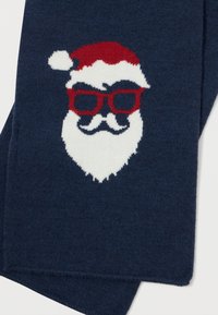 Mørkeblå strikket stof med et hvidt julemandsansigt, der bærer en rød hat og røde briller, samt et hvidt skæg og overskæg.