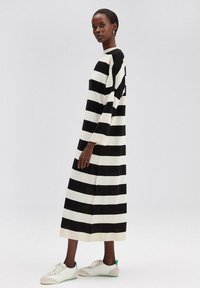 Vestido largo a rayas en blanco y negro con mangas anchas, que presenta un escote redondo y una silueta relajada. Combinado con zapatillas deportivas ligeras.